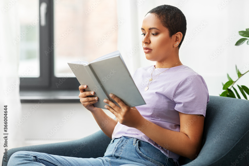 people and leisure concept - african american woman in glasses sitting on sofa and reading book at home people and leisure concept - african american woman in glasses sitting on sofa and reading book at home