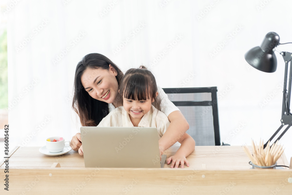 Happiness young mother and daughter sit on a chair in the house, look at laptop for entertain and education, smile and laughing feeling cheerful, family joyful together in the house Happiness young mother and daughter sit on a chair in the house, look at laptop for entertain and education, smile and laughing feeling cheerful, family joyful together in the house