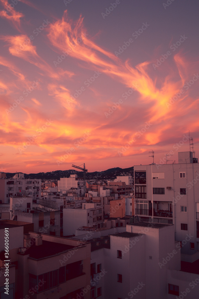 Amazing pink and orange urban sunset in Ibiza town, fire in the sky and pink light reflecting on the town0w buildings. Urban magic summer sunset on the white island.