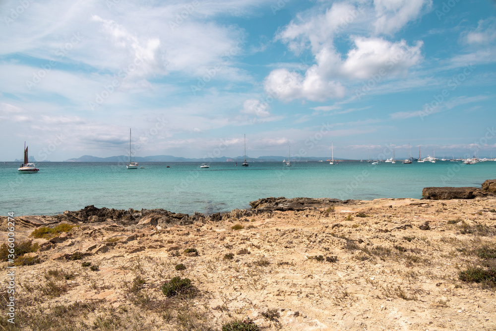 Charming turquoise sea and crystal clear water on the beach of Ses Illetes in Formentera Island, one of the Balearic Islands, Spain. Motor and sail boats in the distance. Mediterranean summer.