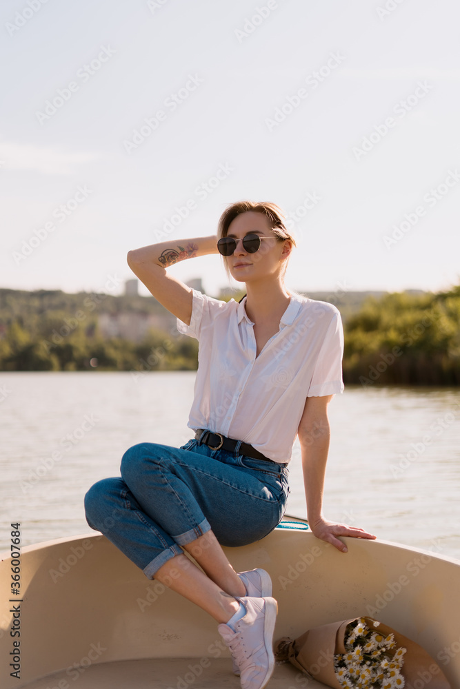 Pretty amazing young woman, blond relaxing on a boat, wearing sunglasses, enjoying her vacation, camomile flowers and amazing time