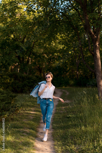 Joyful young woman in fashionable sunglasses walking in nature on a beautiful day
