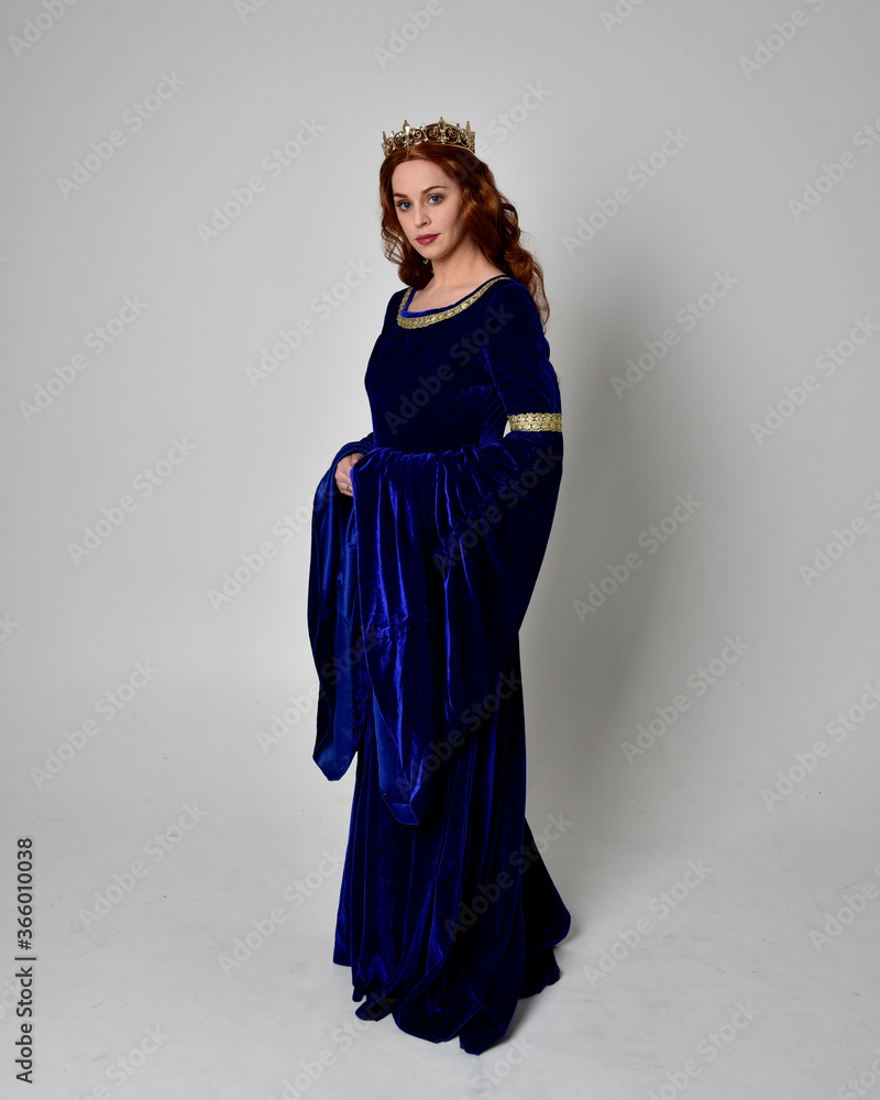 Full length portrait of girl wearing long blue velvet gown with golden crown. standing pose with back to the camera, isolated against a studio background. Full length portrait of girl wearing long blue velvet gown with golden crown. standing pose with back to the camera, isolated against a studio background.