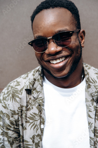 Man's portrait. Close-up portrait attractive young African American man in stylish casual wear and with sunglasses posing outdoors with charismatic smile