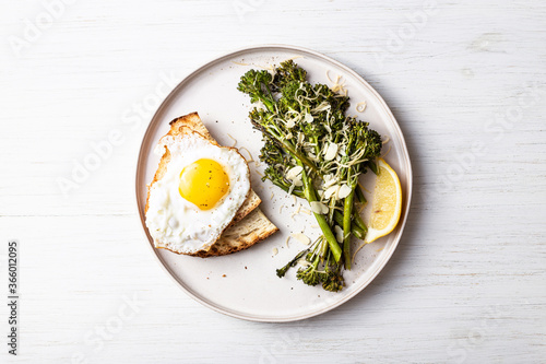 Roasted broccolini, lemon, fried egg with tost on the plate on the table. Top view on healthy food. photo