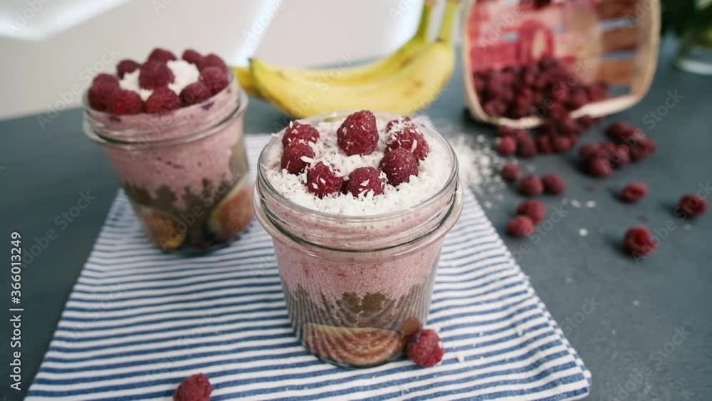 Served glass with healthy smoothie. Smoothie glass decorated with coconut and raspberries. Bananas and berries on the background. View From above. Served glass with healthy smoothie. Smoothie glass decorated with coconut and raspberries. Bananas and berries on the background. View From above.