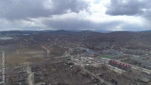 Aerial view of Karabash city with five-story houses and church. In shot construction site, stadium and private houses, Cars drive along the road. Spring, trees without leaves. At the background the Ur