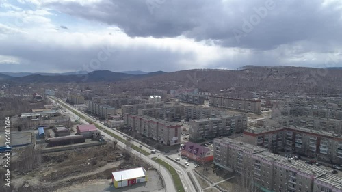 Aerial view of Karabash city with five-story houses. Cars drive along the road. Spring, trees without leaves. At the background the Ural mountains. Russia, Chelyabinsk region
