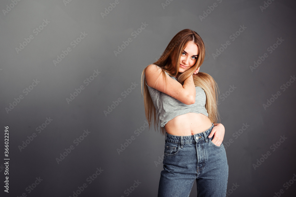 A thin girl with blond long hair looks away and straightens her hair against a dark wall A thin girl with blond long hair looks away and straightens her hair against a dark wall