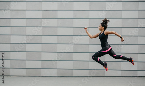 Excellent training running. African american girl in sportswear froze in air above ground, jumping