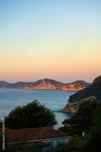 The coast and cliffs of the Greek island Alonnisos are illuminated by the evening sun, seen from the neighboring island Skopelos. © Anna