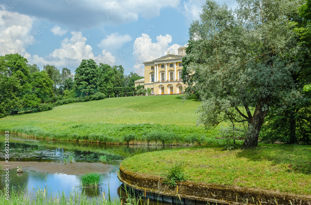 The old Palace stands on a hill in front of a pond and a green meadow surrounded by trees against a blue sky and white clouds