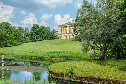 The old Palace stands on a hill in front of a pond and a green meadow surrounded by trees against a blue sky and white clouds