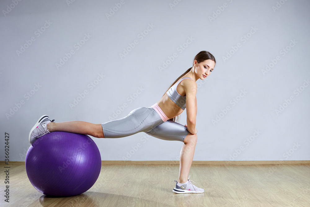 Naklejka premium Young fit woman exercising in a gym. Sports girl is training cross fitness with Pilates Balls.