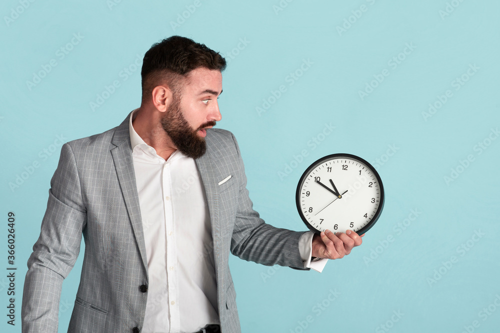 Time management problem. Scared corporate worker with analog clock missing deadline over blue background Time management problem. Scared corporate worker with analog clock missing deadline over blue background