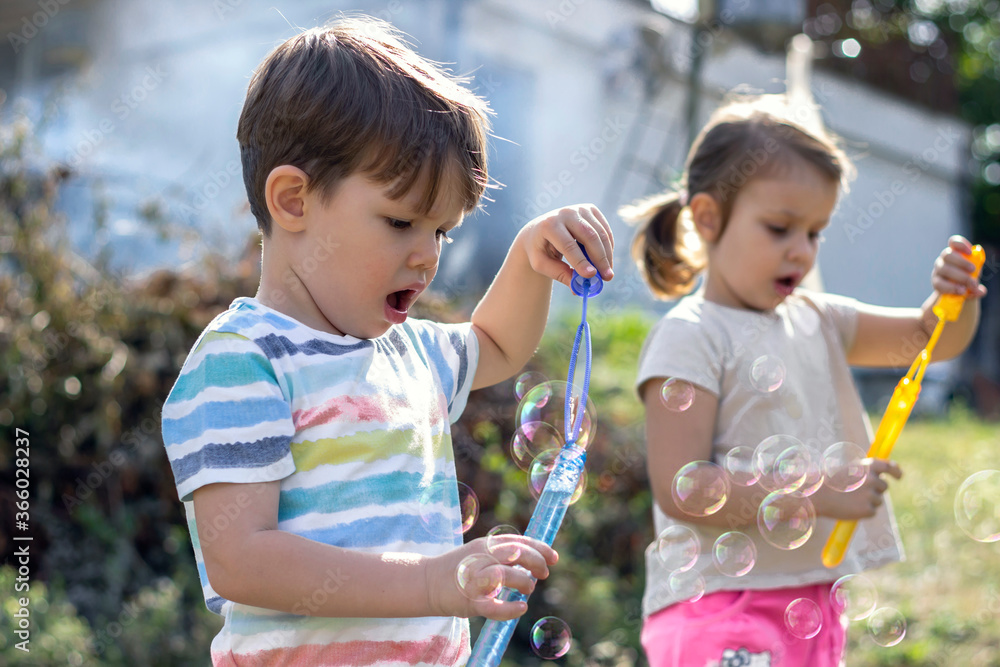 Little caucasian kids boy and girl blowing bubbles in a backyard.Shot ...