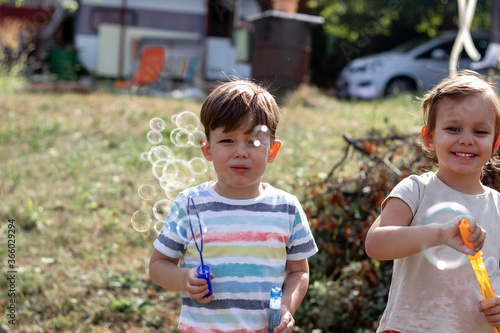 Happy brother and sister playing with bubbles on summer time.Bubbles in the sunset.Children in park blowing soap bubbles and having fun.Two kids in park,green fields,nature background,summer season.