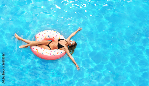 Young Caucasian girl in sexy bikini floating on donut ring at swimming pool, empty space