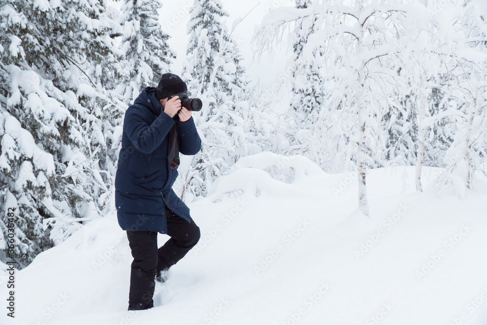 professional photographer or man with camera taking a picture in the snow forest at winter time 
