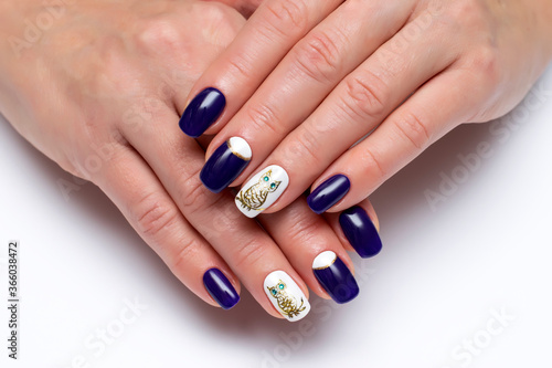 white-blue manicure with a painted golden owl and green eyes on long square nails close-up on a bright background. Dark blue nails.