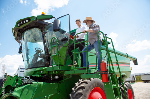 Professional farmer with a modern tractor, combine at a field in sunlight at work. Confident, bright summer colors. Agriculture, exhibition, machinery, plant production. Senior man on his machine with