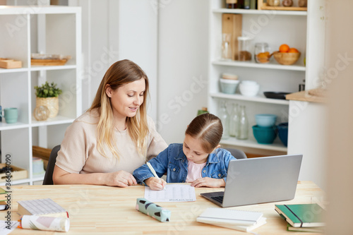 Portrait of smiling adult woman helping girl doing homework or studying at home in cozy interior, copy space