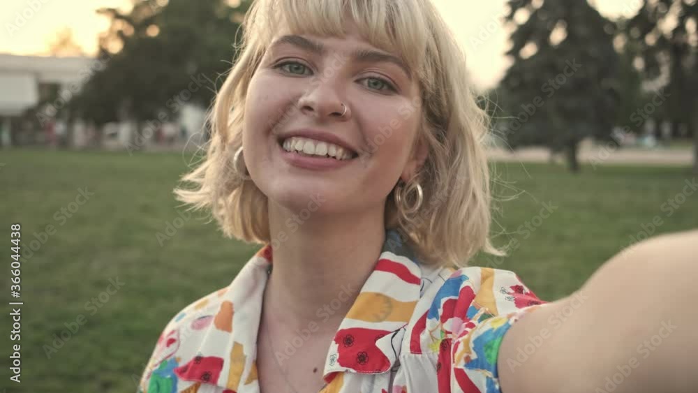 A smiling young woman is recording selfie video in the city park A smiling young woman is recording selfie video in the city park