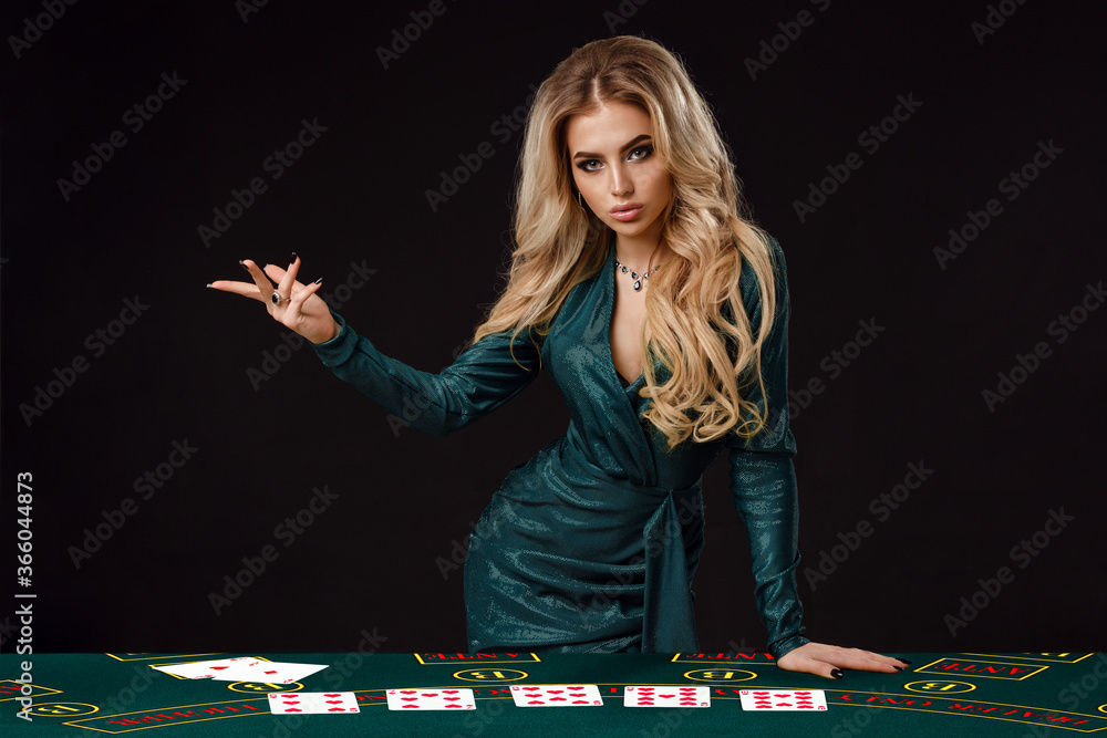 Female in green dress is showing something, leaning on playing table with cards on it, posing on black background. Poker, casino. Close-up, copy space Female in green dress is showing something, leaning on playing table with cards on it, posing on black background. Poker, casino. Close-up, copy space
