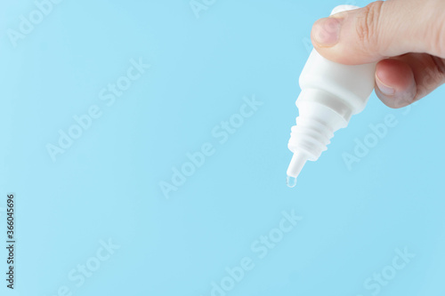 Valokuva Female hand holding eye drop or ear drop bottle with droplet on blue background