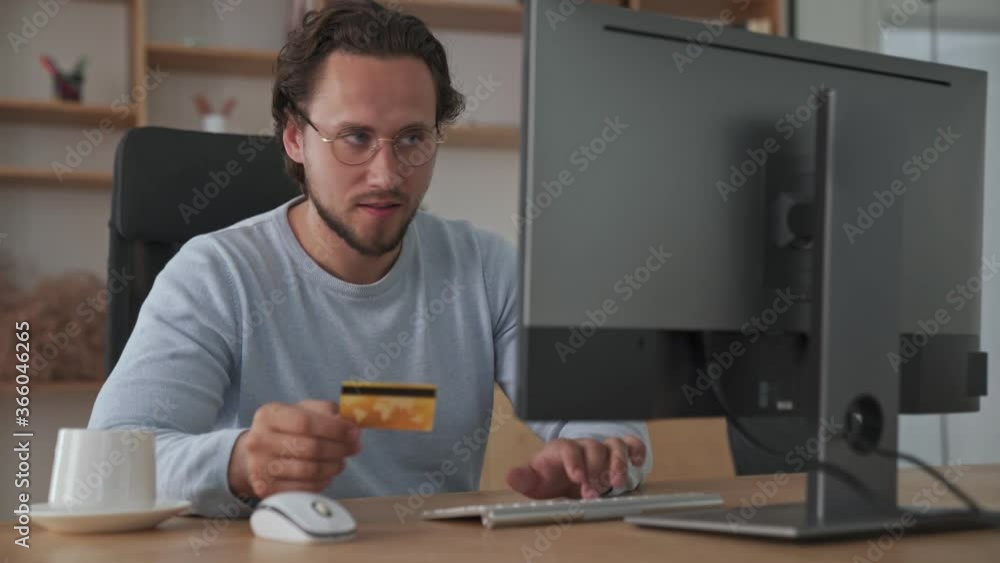 A happy young businessman is using his credit card while using his computer sitting in the office A happy young businessman is using his credit card while using his computer sitting in the office