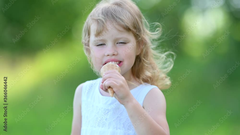 Little Cute Girl in White Summer Dress Enjoying Delicious Ice Cream. Kid with Ice Cream in the City Park. summer family lifestyle. Childhood Little Cute Girl in White Summer Dress Enjoying Delicious Ice Cream. Kid with Ice Cream in the City Park. summer family lifestyle. Childhood