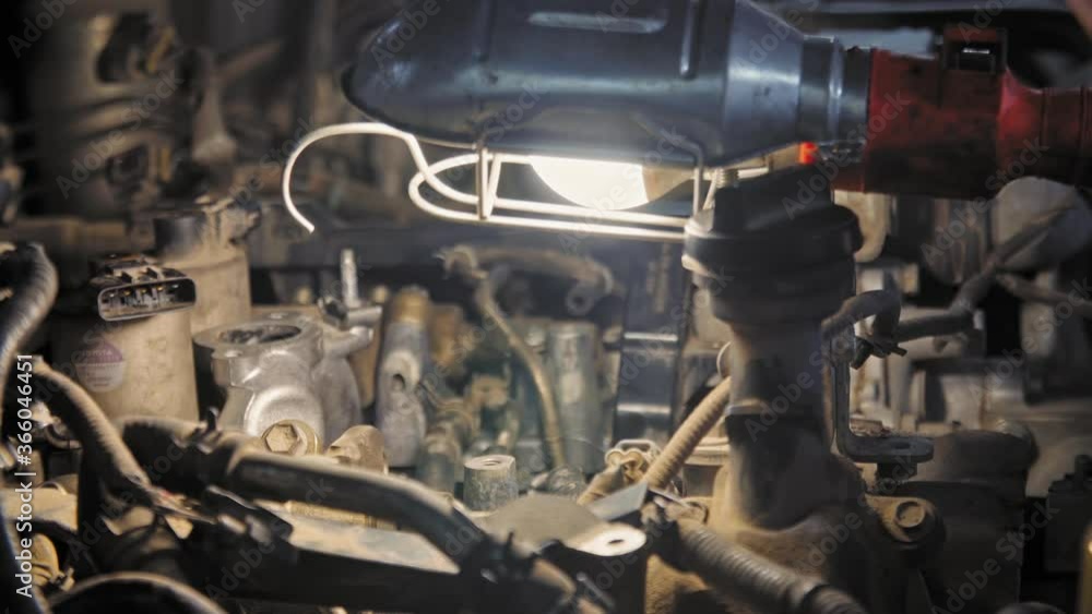 Mechanic repairs the engine with tools and lamp. Close up shot in 4K (UHD)