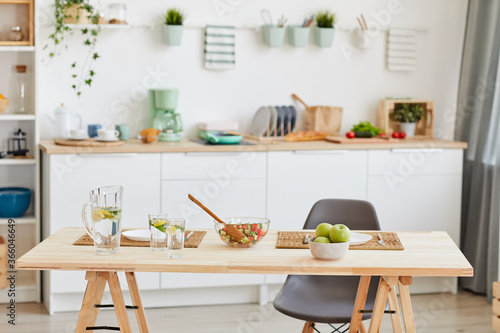 Background image of wooden dining table with fresh food ingredients and salad bowl in cozy kitchen interior  copy space