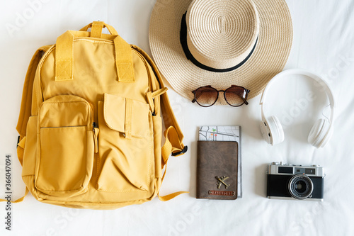 cTravel accessories with beach hat, sunglasses, backpack, camera, headphone and passport on bed at home. Prepare to travel, relaxation, journey, trip and vacation concepts. Top view