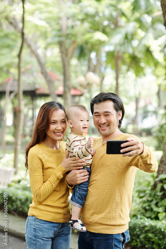 Laughing young parents and their little son laughing when taking selfie together in park © DragonImages