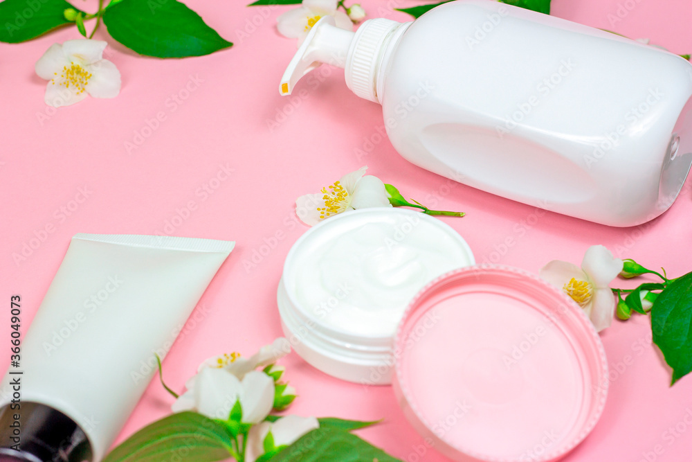White plastic cosmetic container for moisturizing cream as a mock up with bright fresh jasmine flowers on light pink background. Body and skin care, health, wellness and beauty concept.
