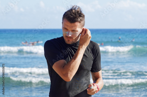 Male Surfer putting sunscreen cream on ear.