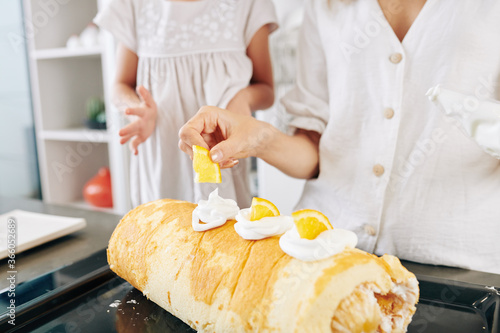 Mother and daughter decorating swiss roll they baked with whipped cream and orange slices