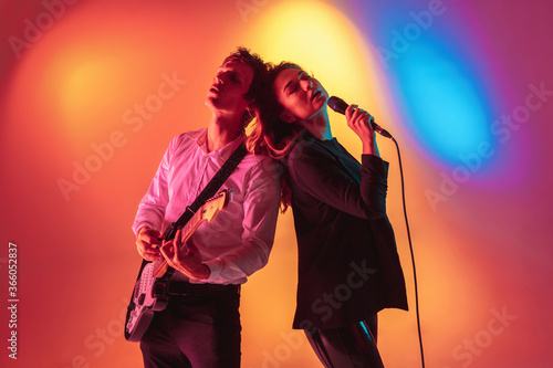 Young caucasian inspired and expressive musician, female singer and guitarist performing on multicolored background in neon. Concept of music, hobby, festival, art. Joyful artist, colorful, bright