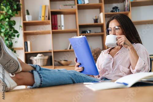 Image of smiling businesswoman drinking coffee and reading documents