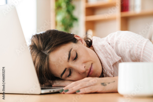 Image of tired adult businesswoman sleeping while working with laptop