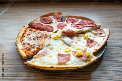 Slices of different pizza with bacon, pepperoni sausages, mushrooms and cheese on a plate and a wooden background