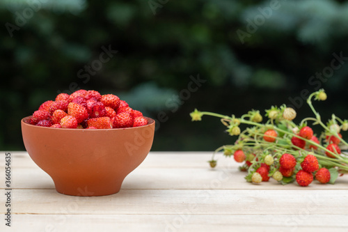 A clay cup with red  juicy strawberries stands on a wooden table