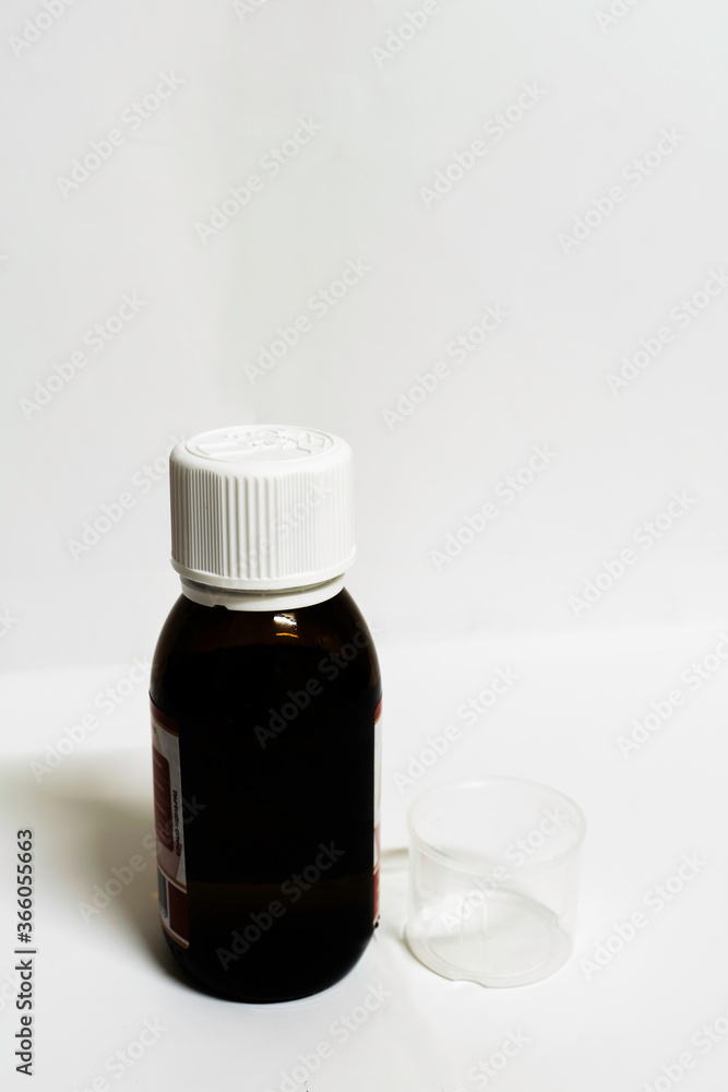 A medicine bottle with empty measurement cup in a white background with spaces for text A medicine bottle with empty measurement cup in a white background with spaces for text