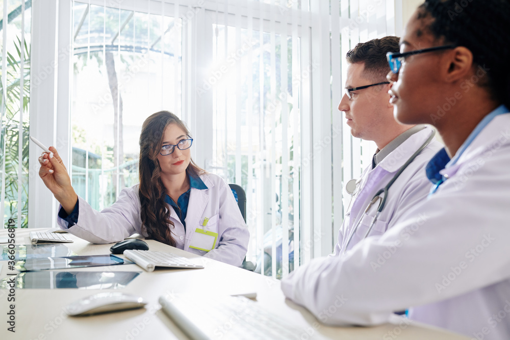 Young female medical scientist pointing at computer screen when explaining results of her research to colleague Young female medical scientist pointing at computer screen when explaining results of her research to colleague