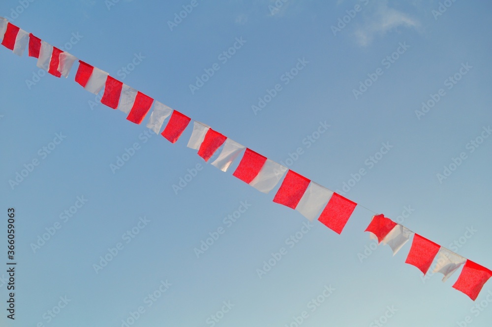 Fototapeta premium Indonesian flag waving in the wind against a blue sky and clouds. Red and white flag. Independence of Indonesia