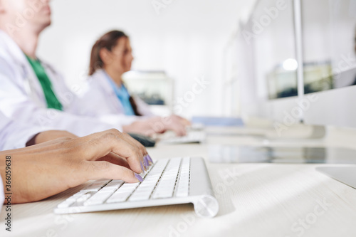 Close-up image of female doctor working on computer in medical office and entering patients data in online form