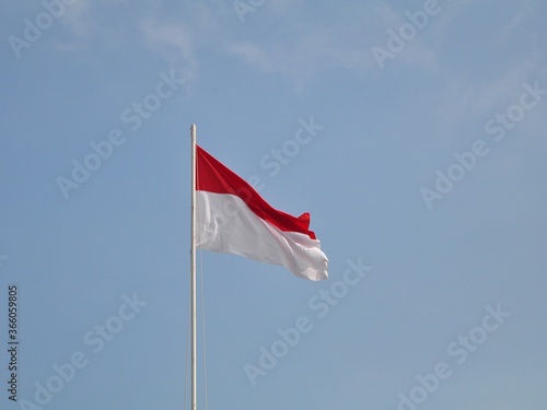 Indonesian flag waving in the wind against a blue sky and clouds. Red and white flag. Independence of Indonesia