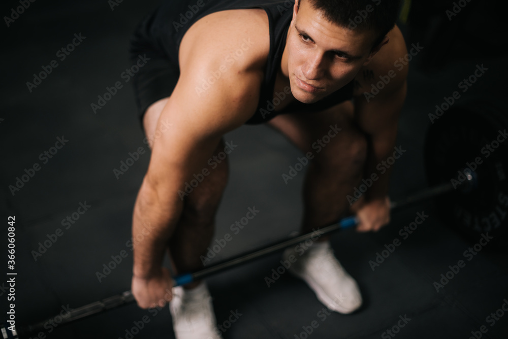 Portrait of Muscular strong man with perfect beautiful body wearing sportswear lifting heavy barbell from floor during sport workout training in modern dark gym. Concept of healthy lifestyle. Portrait of Muscular strong man with perfect beautiful body wearing sportswear lifting heavy barbell from floor during sport workout training in modern dark gym. Concept of healthy lifestyle.