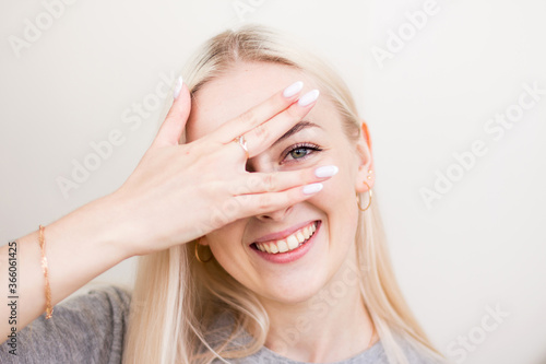 Glad happy young girl with blonde hair, closes eye with hand, prays before important occasion, wishes luck, wishful thinking